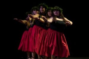 A lineup of Luau dancers with black shirts, red skirts and floral head pieces