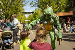 An alien leans over and says hi to children during a parade.