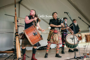 A Celtic band performs on stage. Three drummers and a bagpipe player.