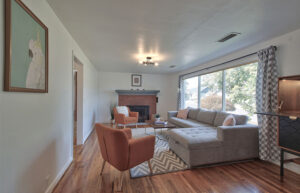 A bright living room with an L shaped sofa and rust colored accent chairs. There is a fireplace.