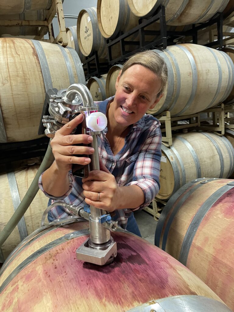 A woman puts an instrument into a wine barrel. She is racking the wine.