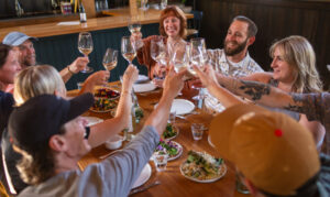 A jovial group sits around a table with their plates full. They cheers their wine glasses.