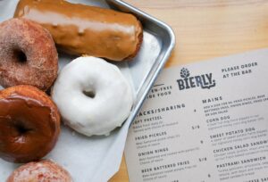 A silver paper lined tray with an array of donuts. It is placed slightly over Bierly's menu, which includes snacks and mains.