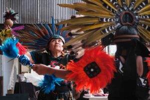 A woman in Mexican dance regalia looks to the sky while dancing.