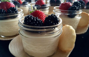 Little jars full of pot de creme with strawberries and blackberries on top.