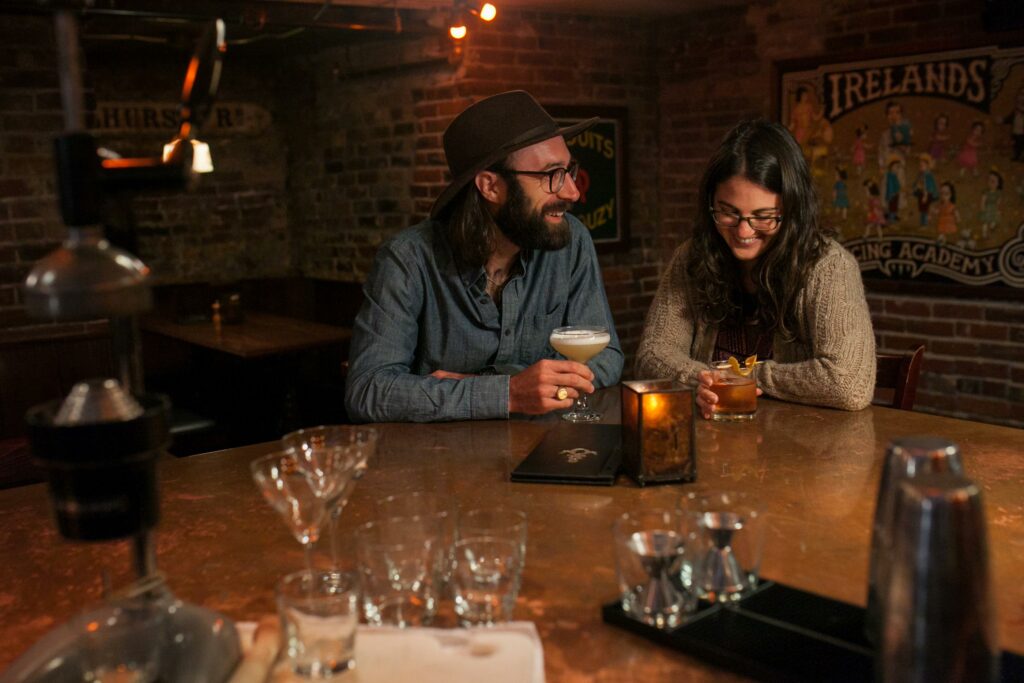 A couple sits at a copper bar with drinks in hand.