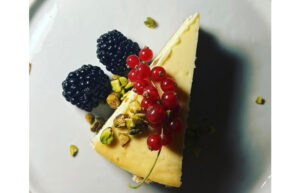 A slice of cheesecake with pistachios, currants and blackberries on top.