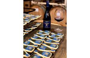 A table filled with wine bottle shaped cookies and a wine bottle with a glass of red wine.