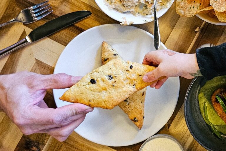 A plate with chocolate chip cookies are in the center of the frame. A child's hand and an adult's hand both grab the same cookie.