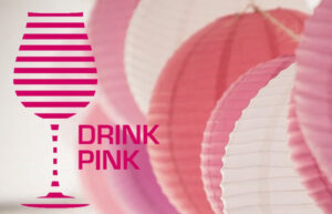 A graphic with a pink wine glass that says Drink Pink. There are paper lanterns of various shades of pink and white in the background.