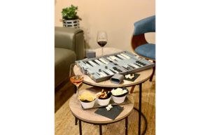 Backgammon game board is set up on a table with a glass of wine and snacks.