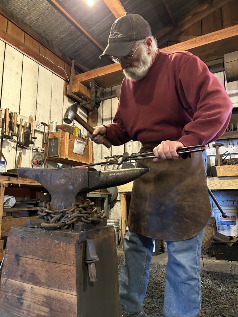 A person with a leather apron hammers on hot metal on an anvil.