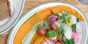 A bright orange spread topped with fresh vegetables and herbs.