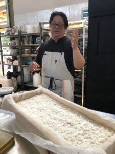 A person in an apron stands behind a tray of white koji.