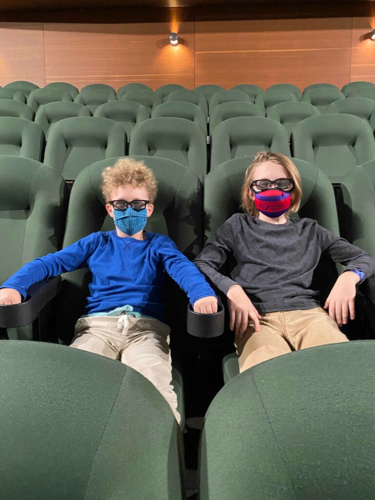 Two kids with 3D glasses on sit in theater chairs.