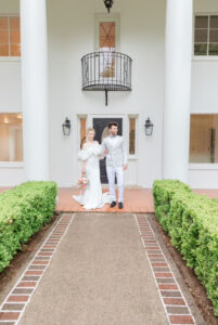 A bride and groom stand in front of a large plantation style front entrance.