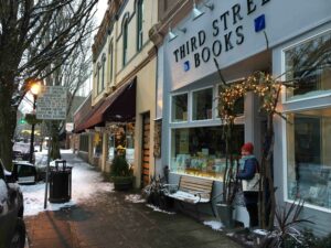 A person with a red beanie hat and a blue puffer coat steps outside of a retail business called Third Street Books.