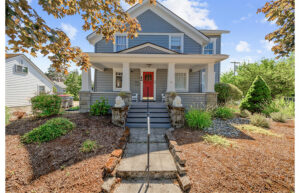 A blue craftsman style home with a large front porch and lion guardians at the entrance.