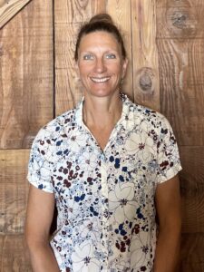 A woman stands in front of a large wooden barn door and smiles.