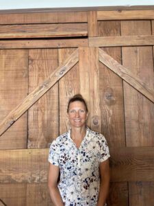 A woman stands in front of a large wooden barn door and smiles.