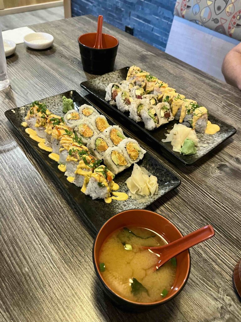 Two rectangular plates full of sushi and two bowls of miso soup.