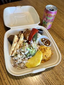A compostable to-go box filled with food and a can of Hawaiian Sun juice.