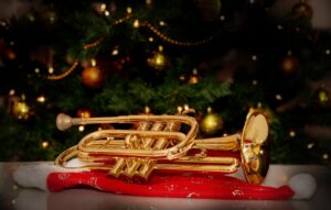 A gleaming trumpet is set underneath a Christmas tree.