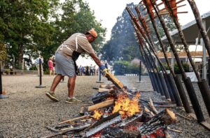 A man leans over a large long fire and tends it.