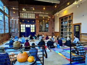 A group of people sit on yoga mats in a beautiful room.
