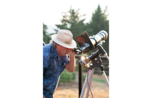 A man with a white hat looks through a telescope.
