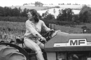A woman operating a tractor looks behind her as she backs it up.