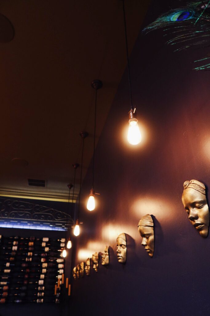 Gold painted realistic face sculptures hang on an eggplant colored wall.  Each gleaming gold face has closed eyes.