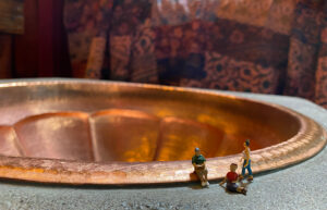 Three tiny people figurings are placed in front of a copper sink.