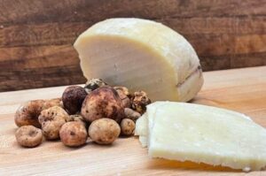 A block of hard cheese and a handfull of truffles are on a wood cutting board