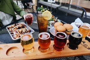 An outdoor table is set with a colorful flight of beer, tacos, sliders, and salad.