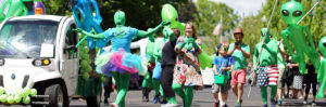 People dressed as aliens walk and dance in the street for a parade.