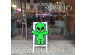 A storefront that says Apollo Art Collective. There is an alien pasted on a sandwich board sign.
