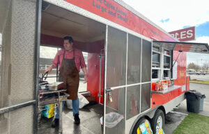 A man stands in front of a grill as he cooks food inside an open and airy red food truck.