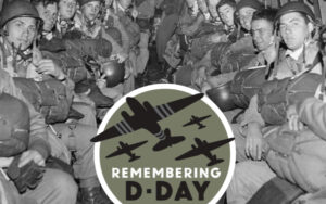 A photo of men lined up sitting on benches. They have armed forces gear. An overlay says Remembering D-Day.