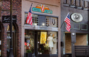 The outside storefront of a vintage store. Two American flags are on either side of a sign that says Vintage on Third.