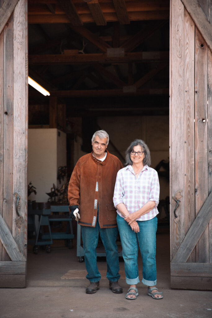 Two people stand and smile in front of a large open sliding barn door.