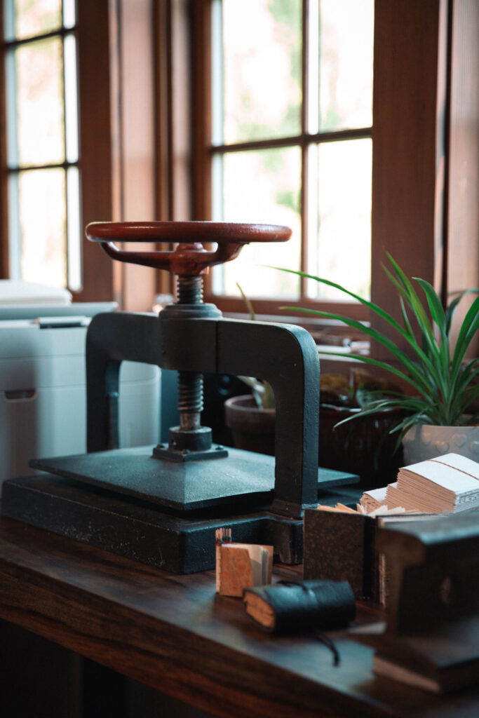 A vintage book press with small leather bound books scattered around it.