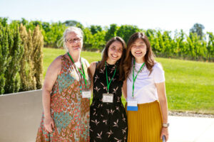 Three smiling women with lanyards have their arms around each others' shoulders.