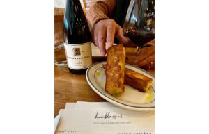 There is a plate with toasted bread and a person is reaching for a piece. There is a bottle of Youngberg Hill wine next to the plate.
