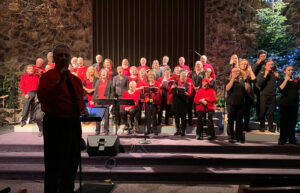 Choir members with red shirts stand on risers as they sing.