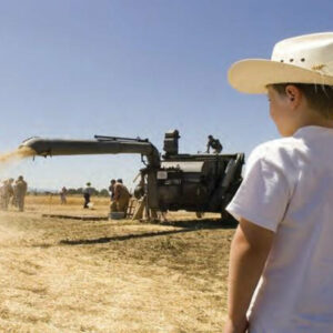 A kid with a cowboy hat watches a demonstration of a harvester.