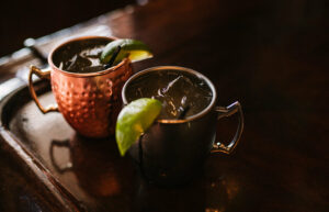 Two Moscow Mule drinks in copper mugs with limes on the rim.