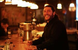 A person stands at the bar and smiles at the camera.